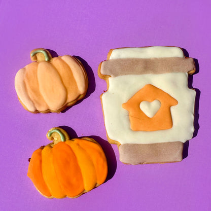Decorative cookies shaped like pumpkins and a coffee cup with a heart cutout on a purple background