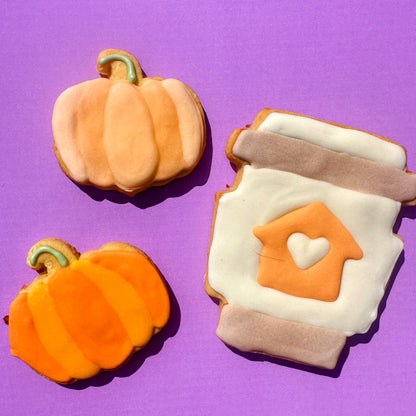 Two pumpkin-shaped cookies and a mug-shaped cookie with a heart on a purple background