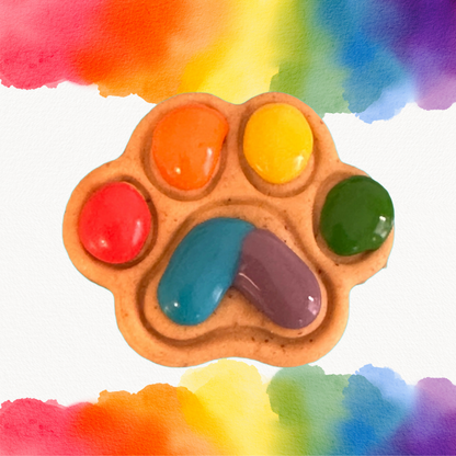 A dog treat shaped like a paw with multicolored icing resembling a rainbow on a watercolor background.