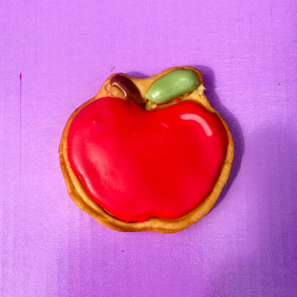 Red apple-shaped cookie with a green leaf on a purple background