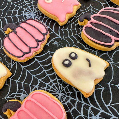 Halloween-themed cookies decorated like ghosts and pumpkins on a spider web background.
