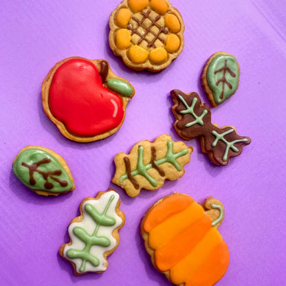 Decorative cookies shaped like an apple, sunflower, leaves, and pumpkin on a purple background