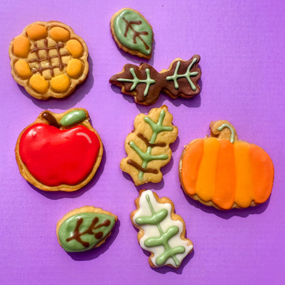 Decorative cookies shaped like a corn cob, apple, leaves, and pumpkin on a purple background