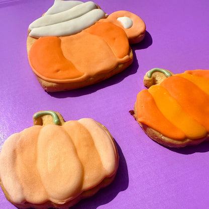 Pumpkin-shaped cookies with orange and beige icing on a purple background