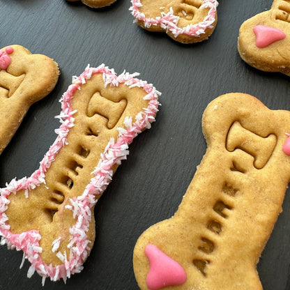 Bone-shaped dog biscuits decorated with white and pink icing, on a black surface.